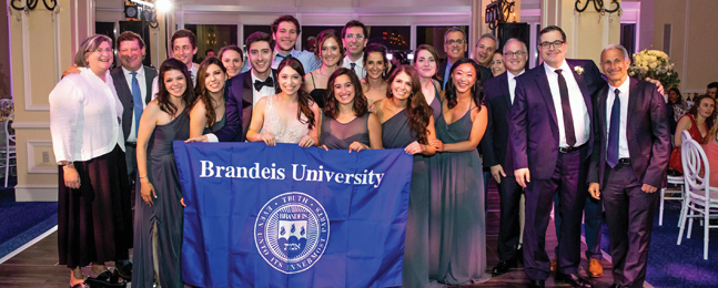 Large group of people, a bride and groom, stand behind a large Brandeis banner.